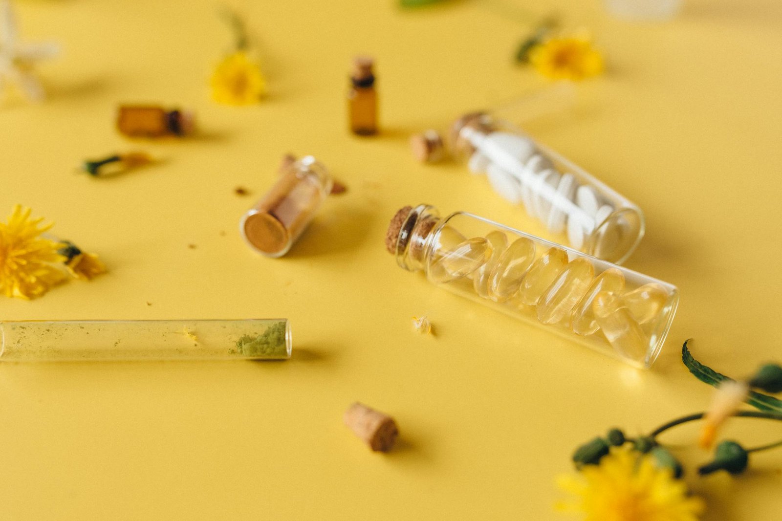 Assorted herbal supplements and pills in glass vials on a vibrant yellow surface.